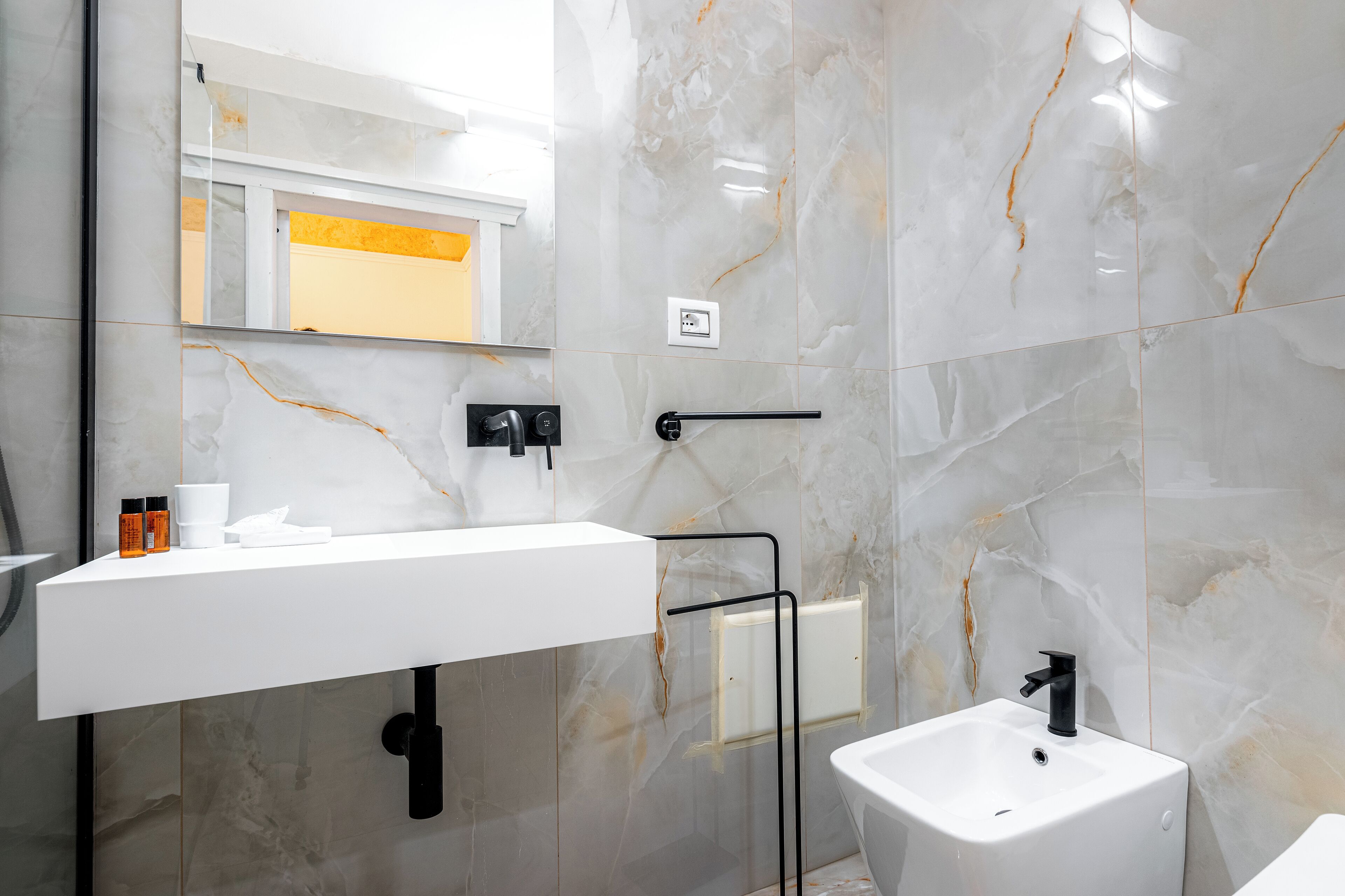 A modern bathroom with a white sink, black faucet, and marble walls.