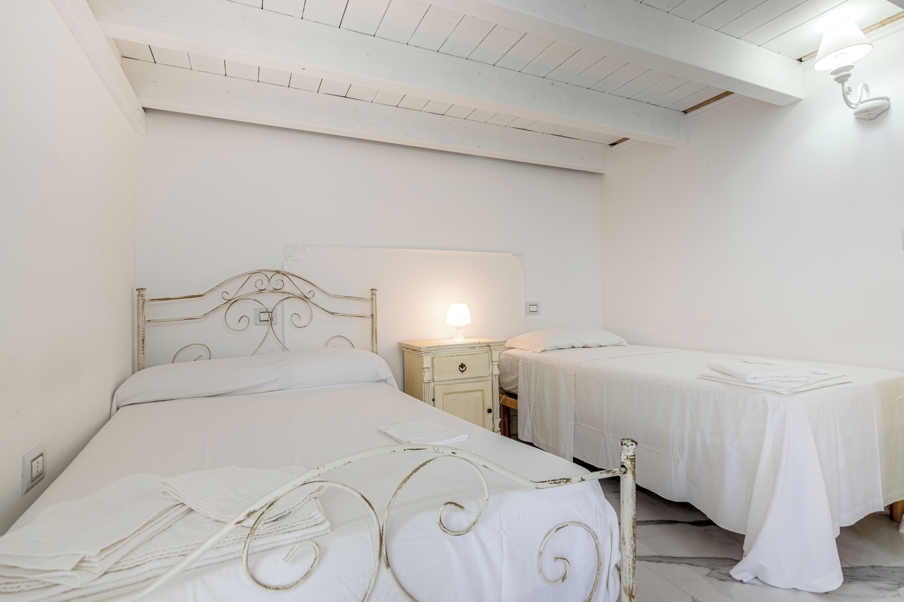 Ein Zimmer mit zwei Betten, einem Nachttisch mit Lampe und einer weißen Decke.