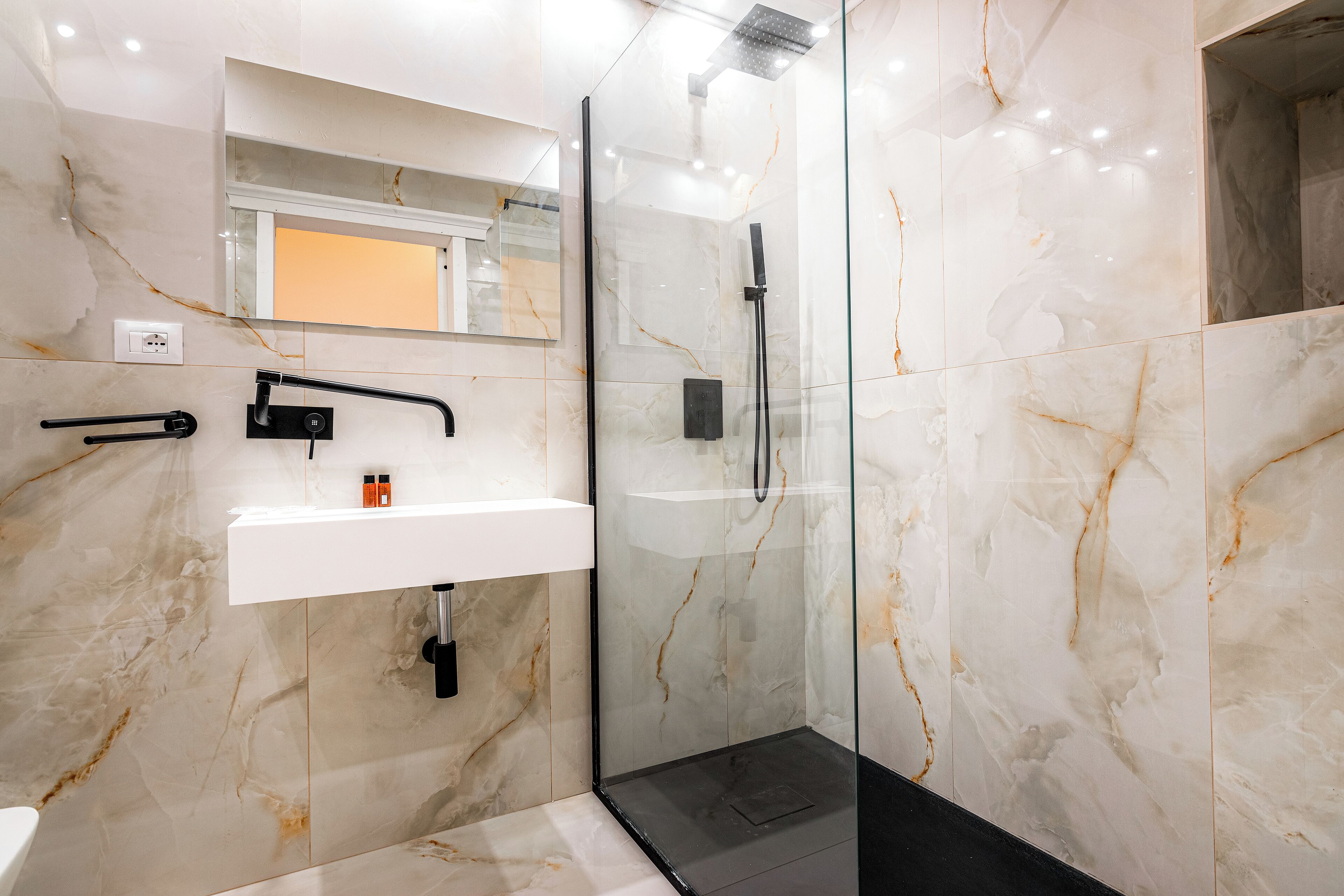 A modern bathroom with a glass-enclosed shower, a white sink, and a marble-tiled wall.