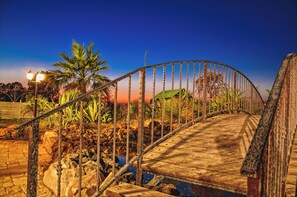A wooden bridge with metal railings, surrounded by rocks and plants, under a clear sky.