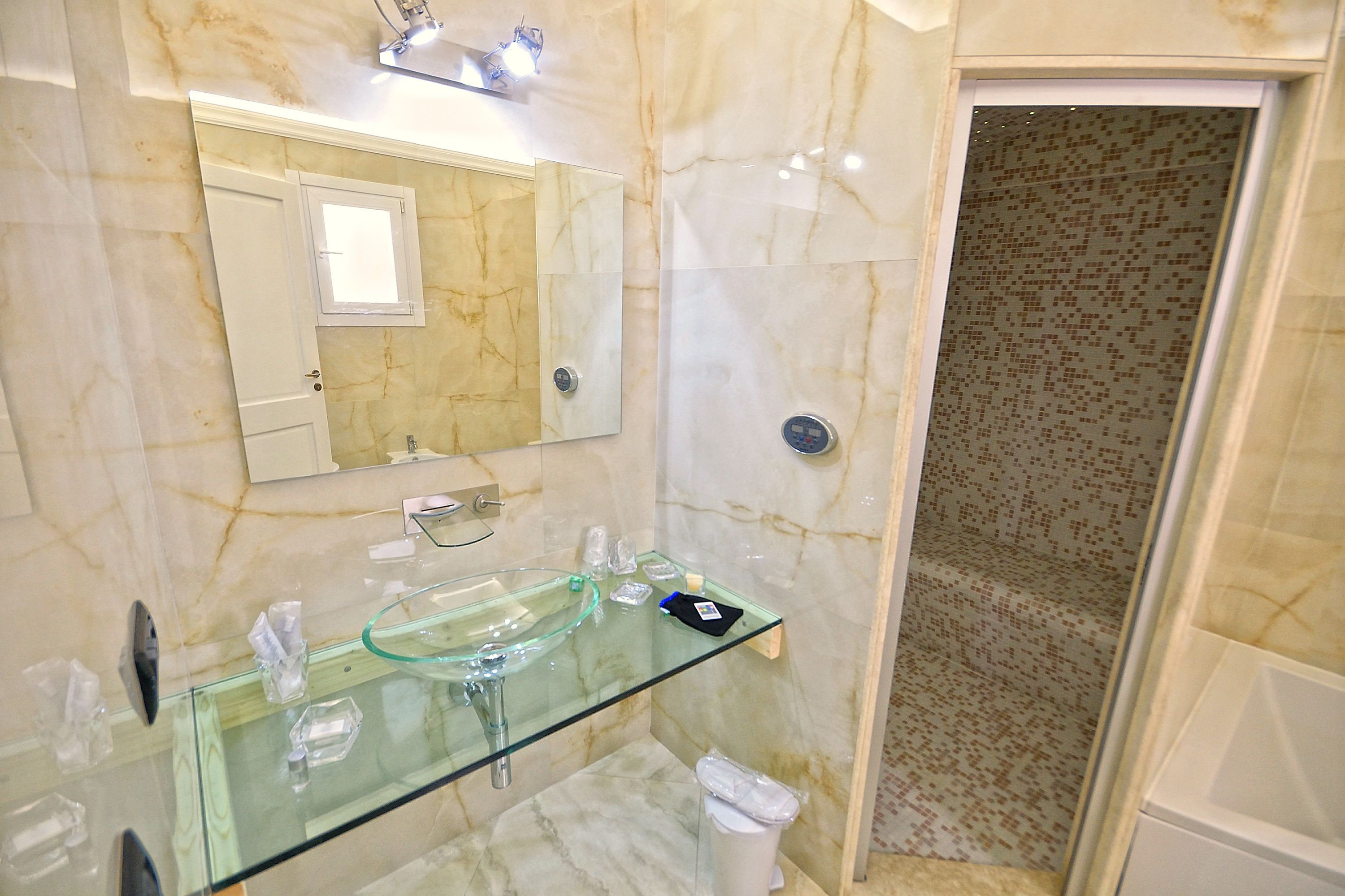 Een badkamer met een glazen wastafel, een spiegel en een douchegedeelte.