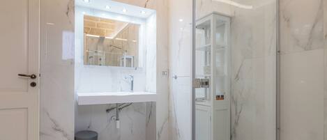 Une salle de bain moderne avec un lavabo en marbre, une cabine de douche en verre et une poubelle visible.