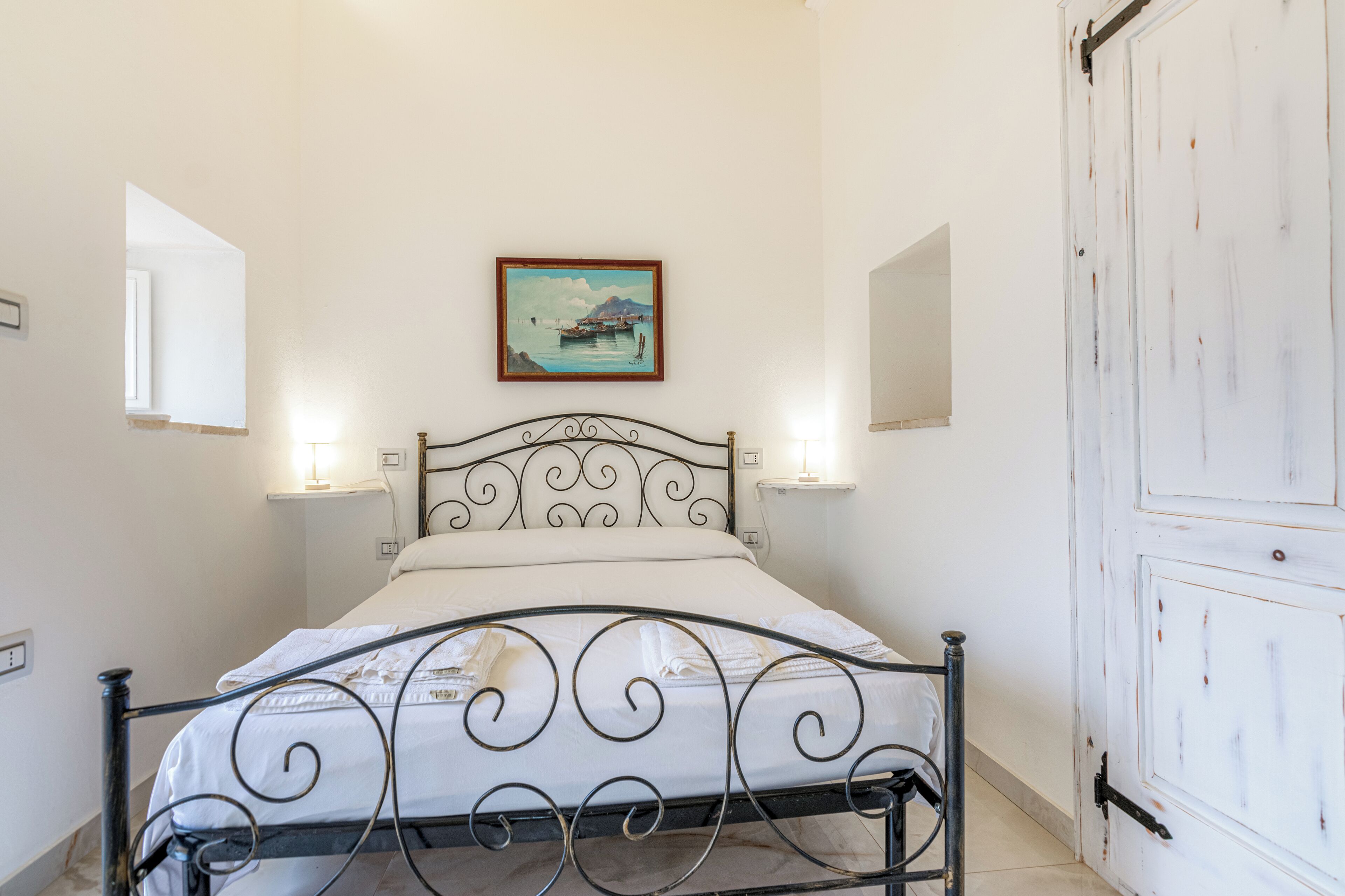 A bedroom with a metal bed frame, a painting on the wall, and a white door.