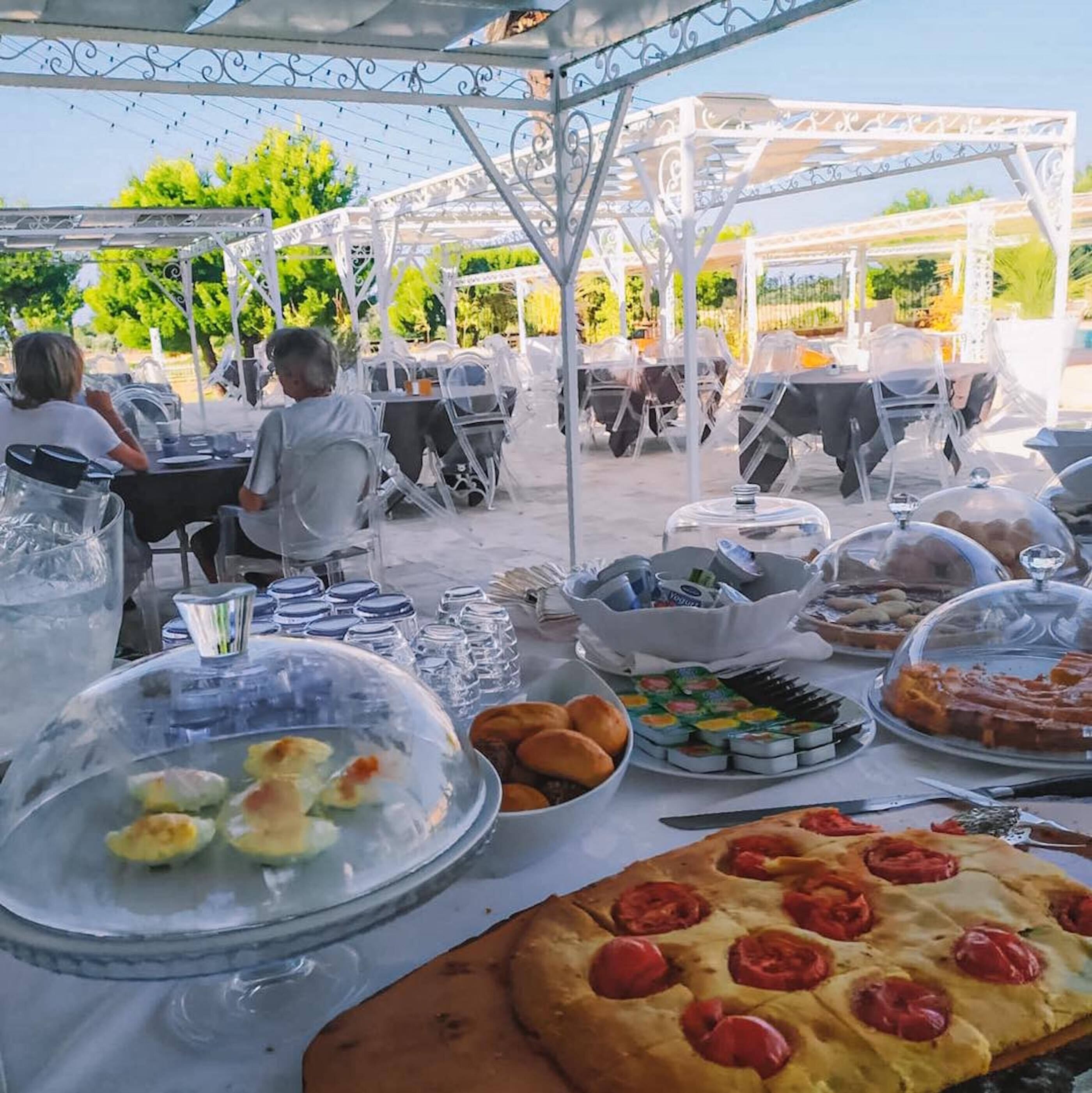 An outdoor dining area with covered tables, food and drink containers, and a pizza.