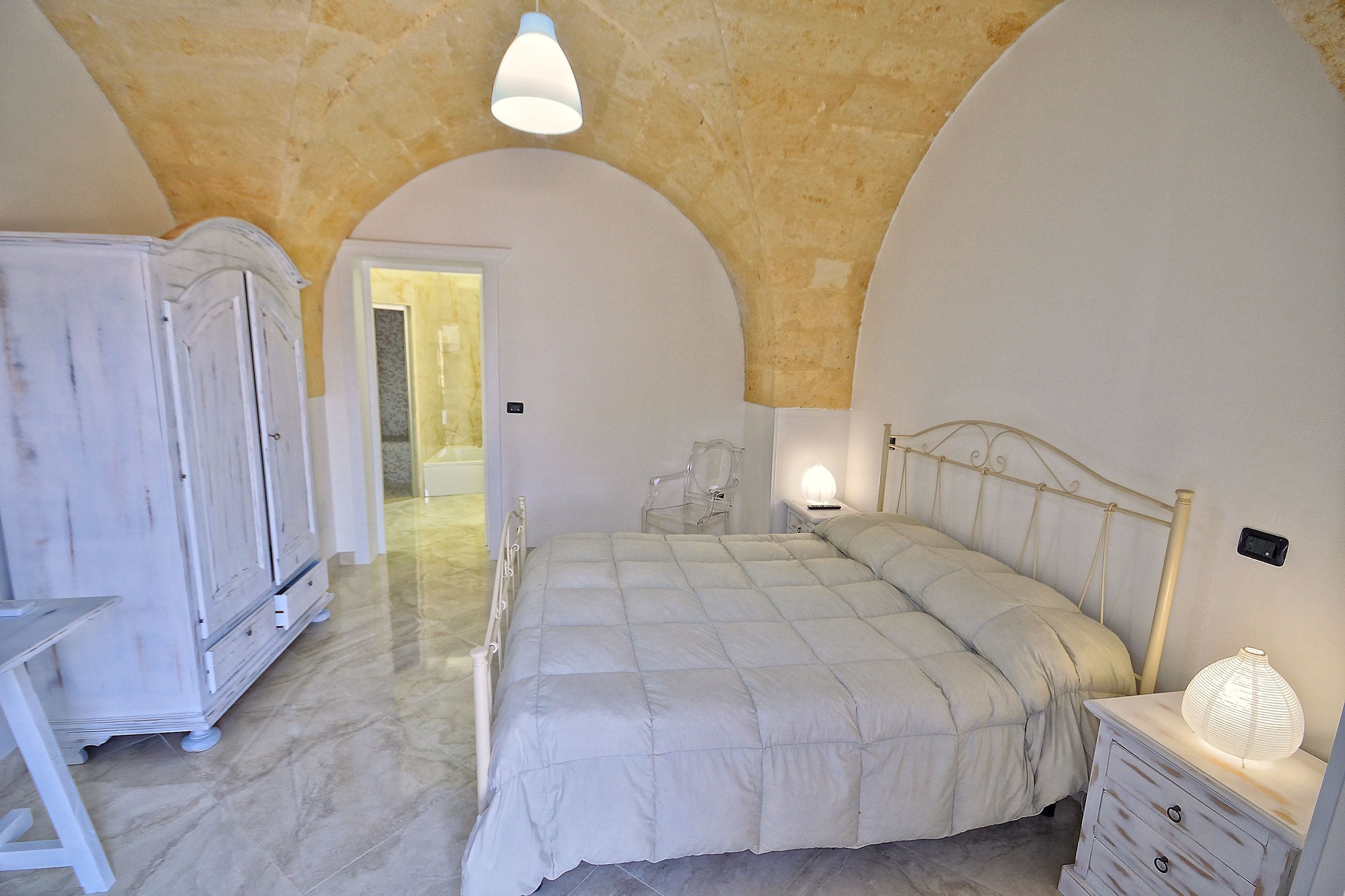 A bedroom with a bed, dresser, and arched ceiling.