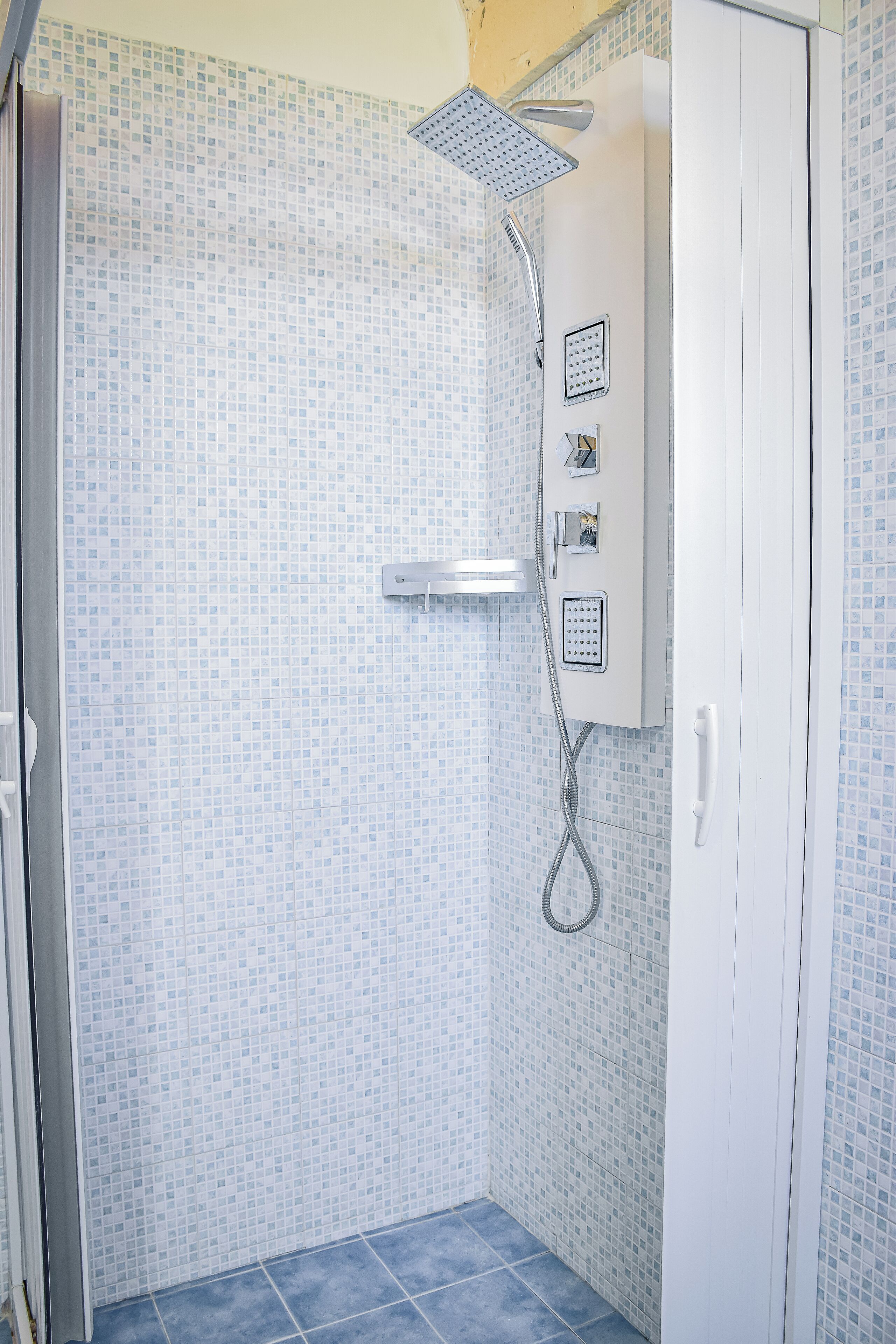A shower area with a tiled wall, a showerhead, and a control panel.