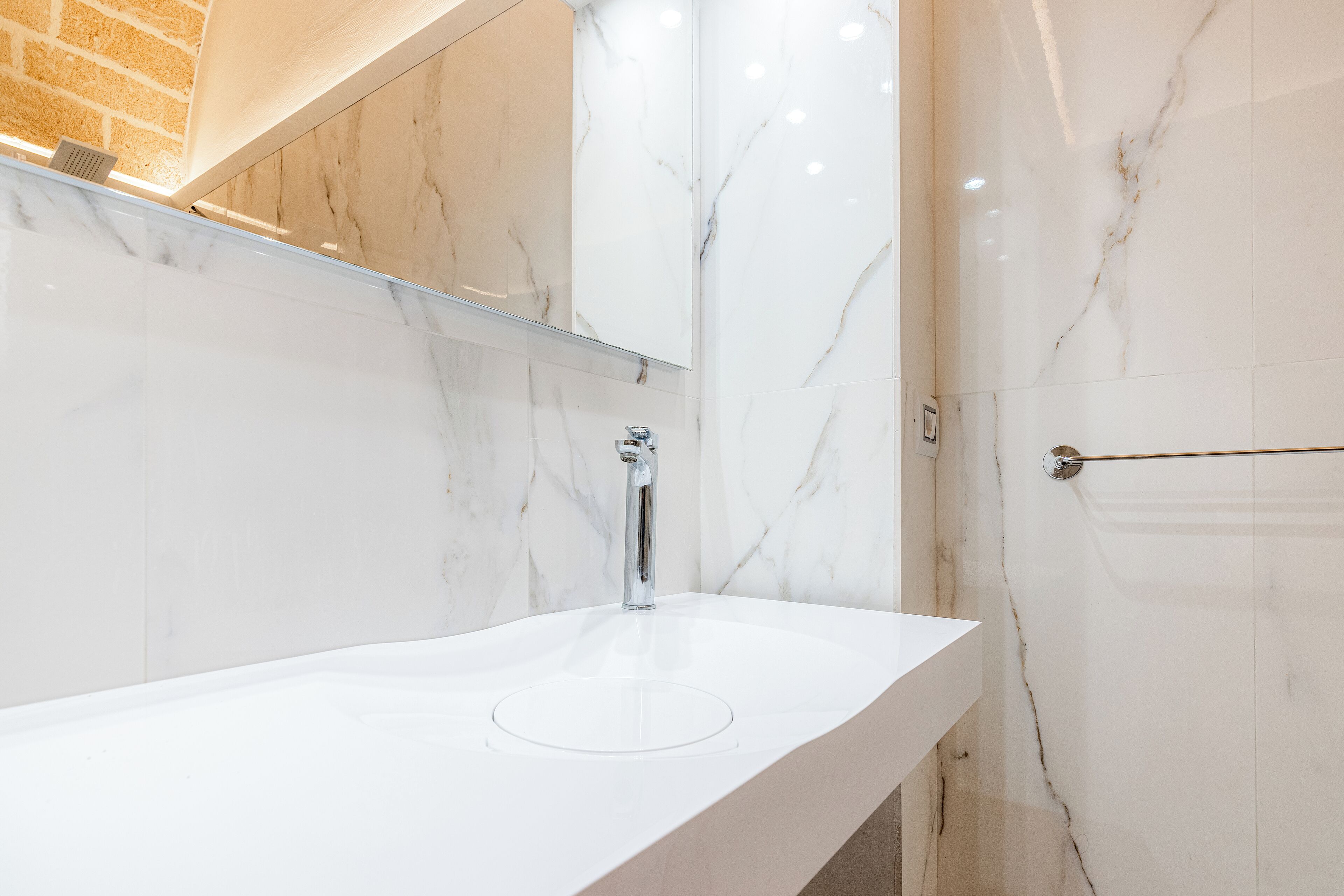Un baño moderno con lavamanos de mármol blanco, grifo cromado y un espejo grande.