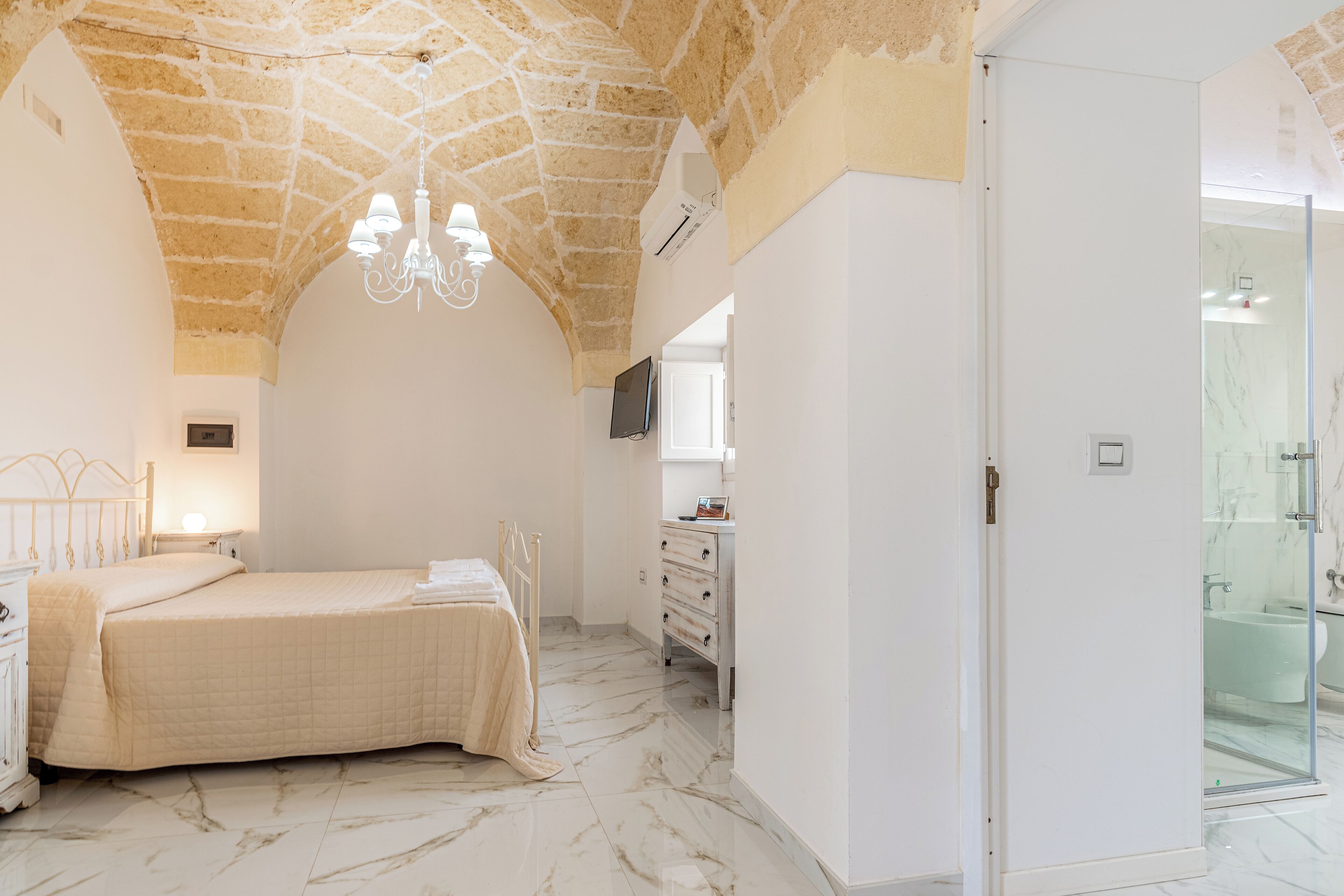 A bedroom with a bed, a dresser, a vanity, and a shower area.