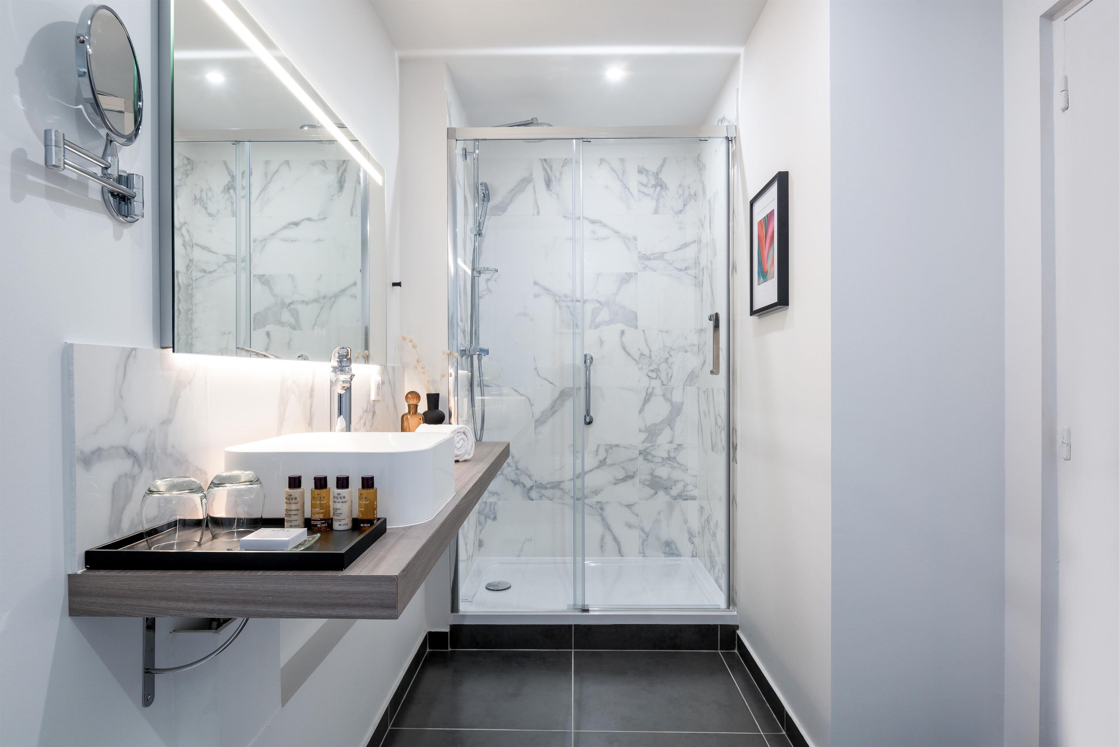 Un baño moderno con tocador de mármol, cabina de ducha de vidrio y un cuadro en la pared.
