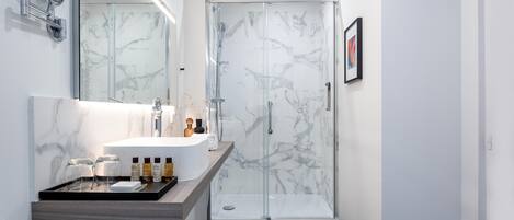Un baño moderno con tocador de mármol, cabina de ducha de vidrio y un cuadro en la pared.