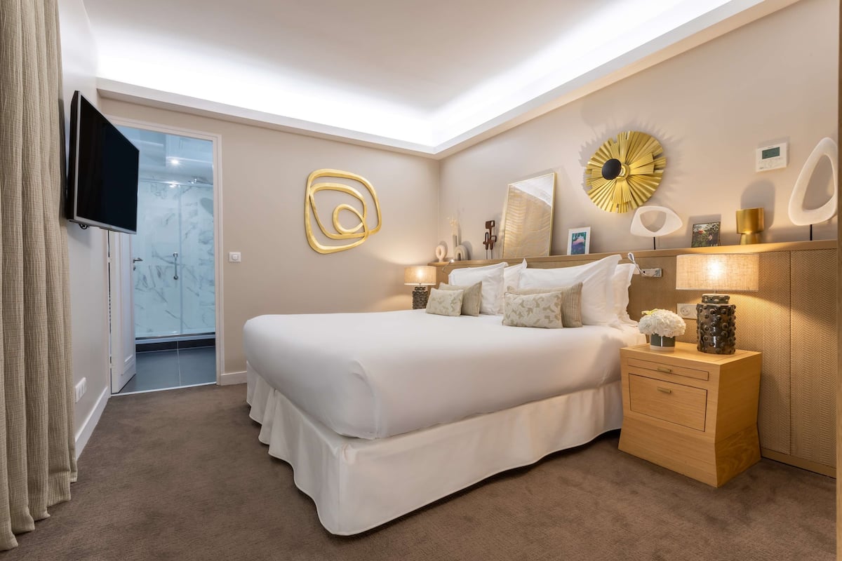 Un dormitorio moderno con una cama grande, mesitas de noche, un televisor y decoración mural.