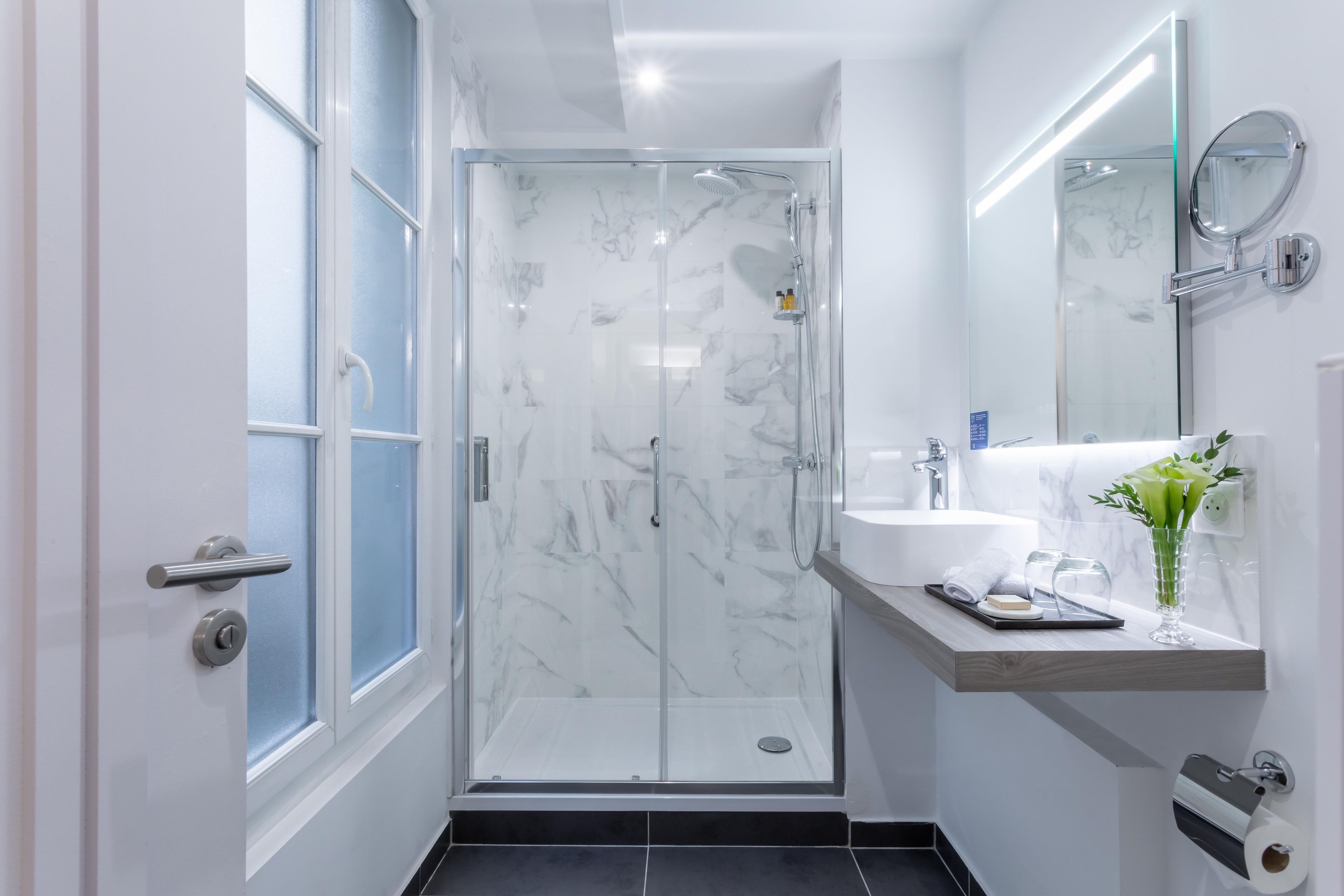 A modern bathroom with a glass-enclosed shower, a white sink, and a mirror above it.