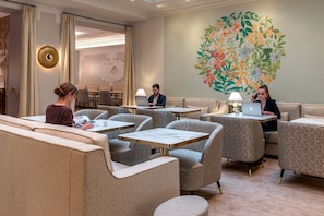 Ein moderner Lounge-Bereich mit Sitzgelegenheiten und Tischen, einer großen Blumenwand und einer runden Wandleuchte.