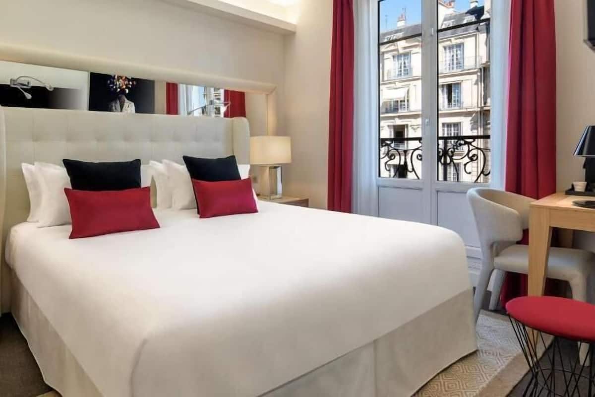 Una habitación de hotel con una cama grande, dos mesitas de noche, un escritorio y una silla.