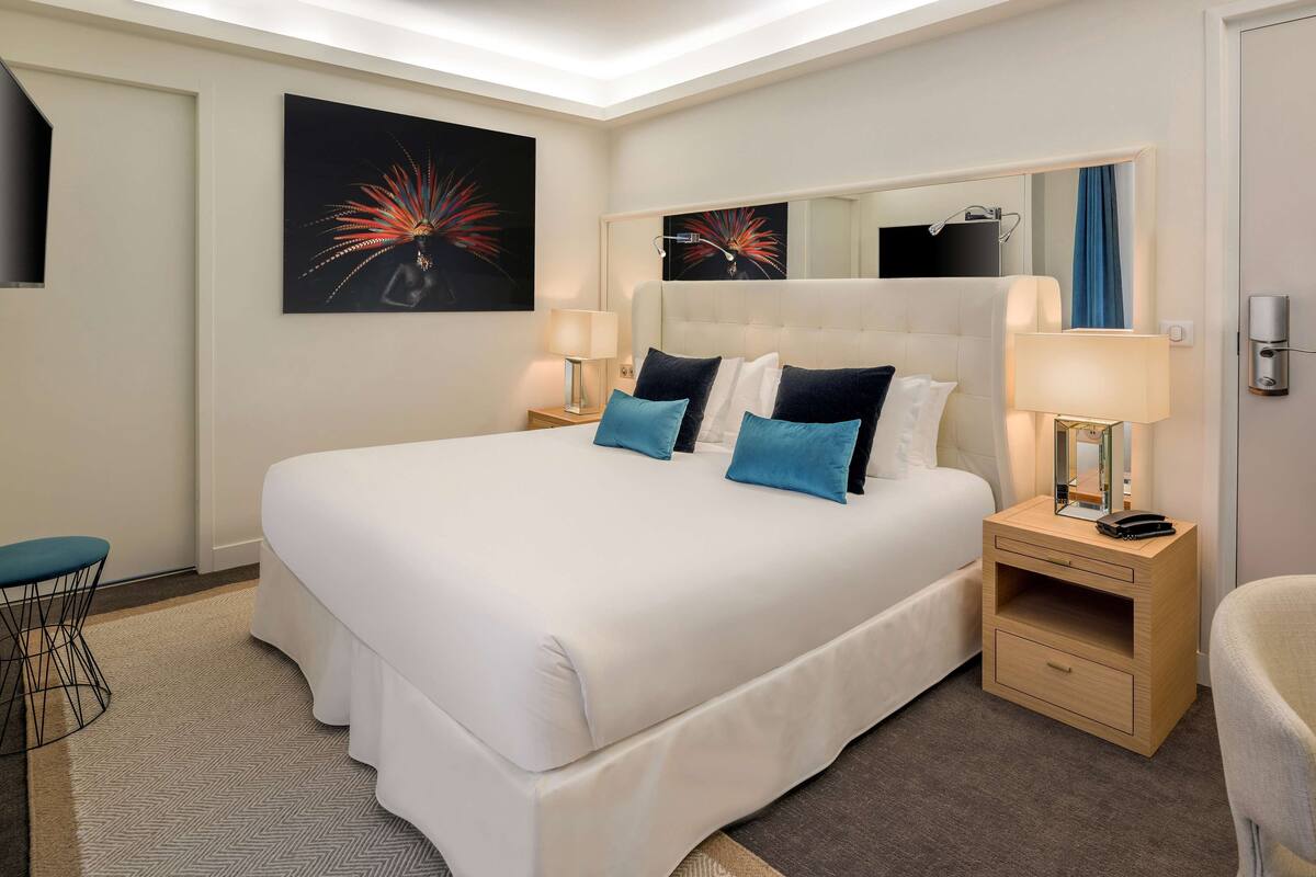 Una habitación de hotel con una cama grande, dos mesitas de noche, una silla y obras de arte en las paredes.
