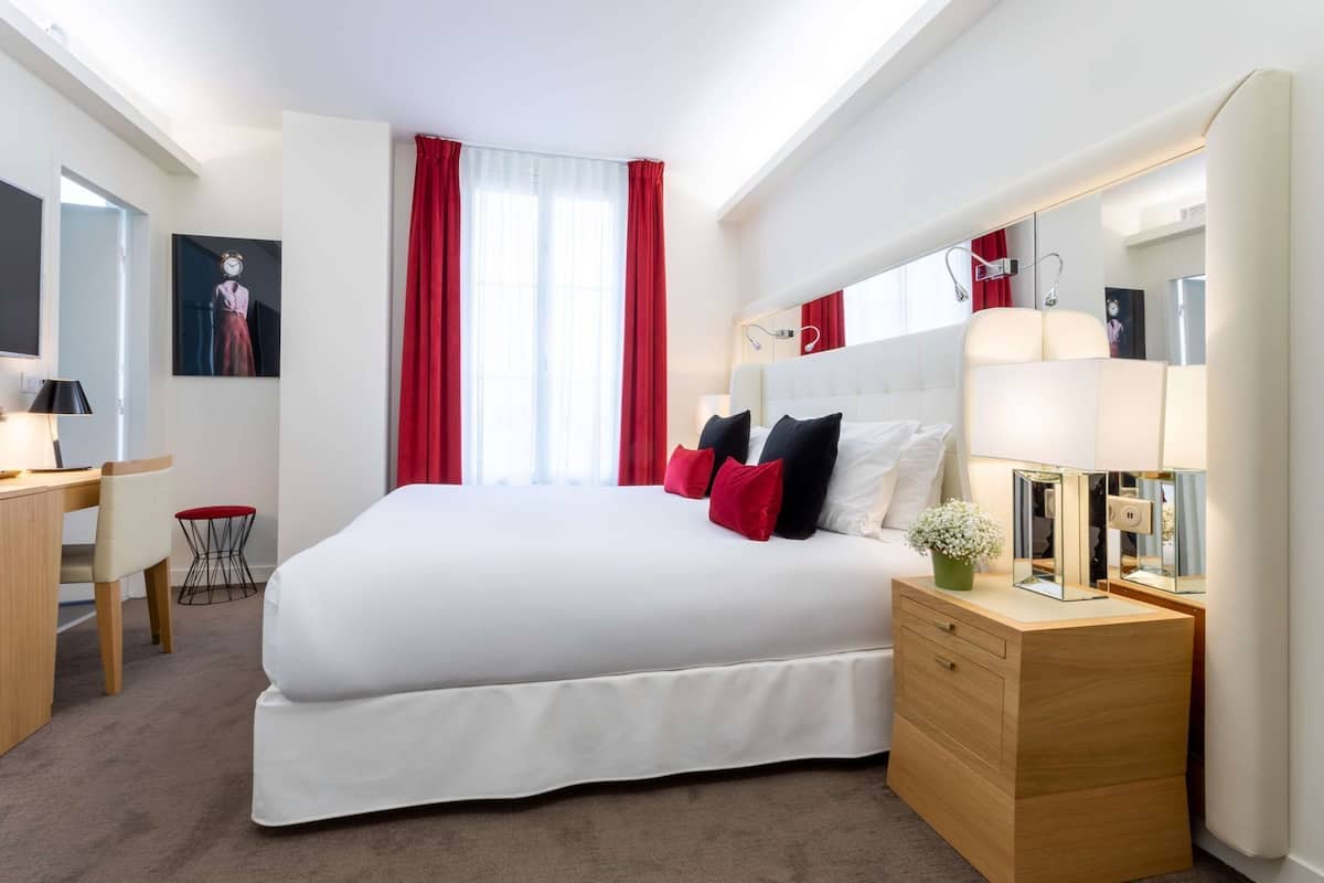 Una habitación de hotel con cama, mesita de noche, lámpara y escritorio con silla.