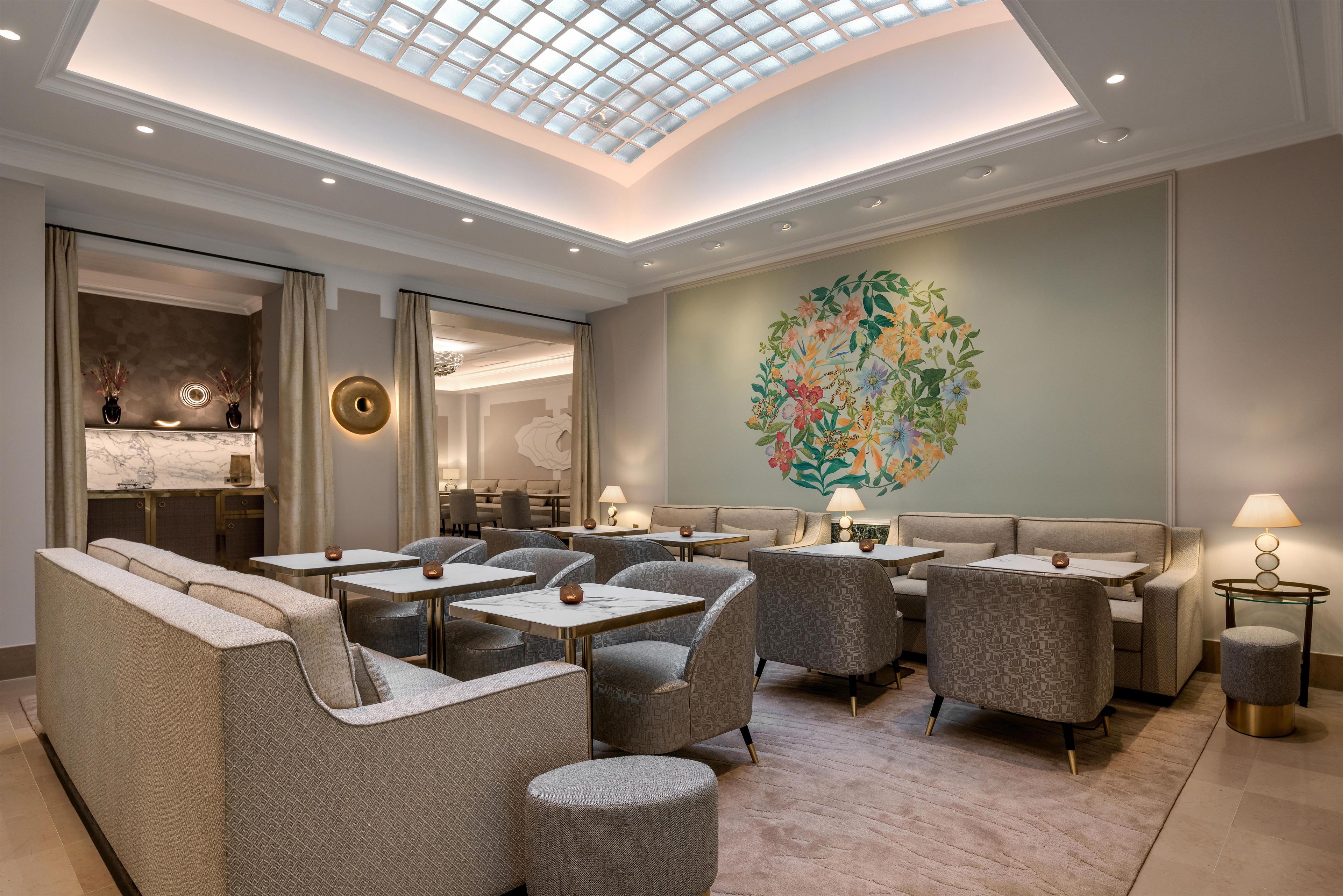 Eine Hotelhalle mit hoher Decke, eingelassener Beleuchtung, Sitzgelegenheiten und einem großen floralen Wandbild.