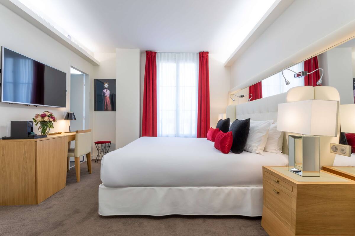 Una habitación de hotel moderna con una cama grande, un escritorio, un televisor y un espejo.