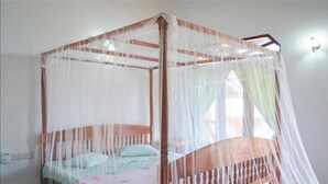 A four-poster bed with a mosquito net, a wooden headboard, and a bedspread with a floral pattern. - Coppenrath (Tangalle)