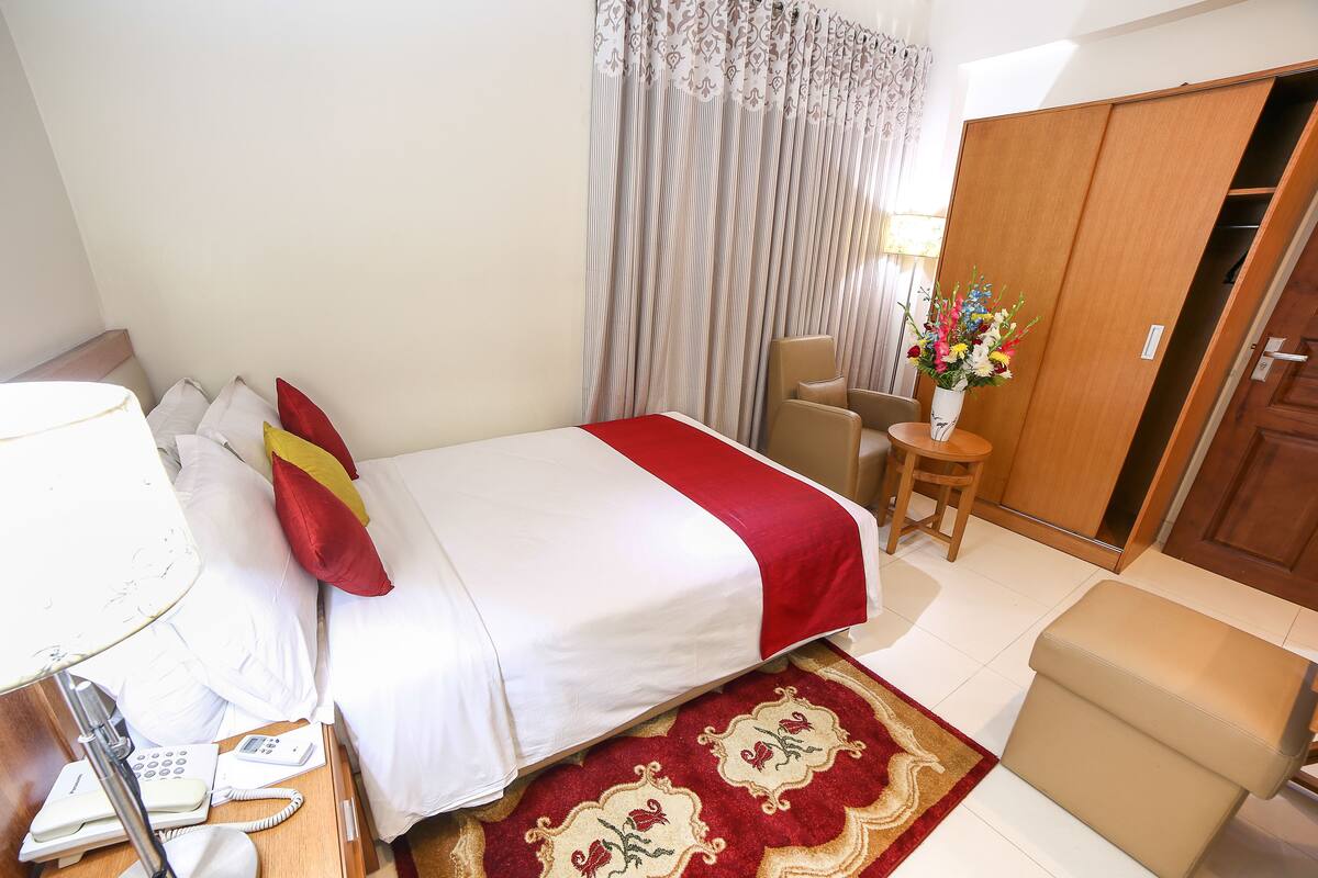 A hotel room with a bed, bedside table, lamp, phone, chair, and a wardrobe.