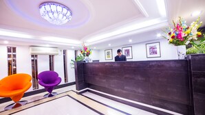 A reception area with a dark reception desk, two colorful chairs, and a chandelier. - Nascent Gardenia Suites (Dhaka)