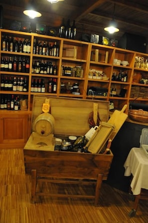 Um barril de madeira dentro de uma caixa de madeira com formato de barril, rodeado por prateleiras com garrafas de vinho e copos.