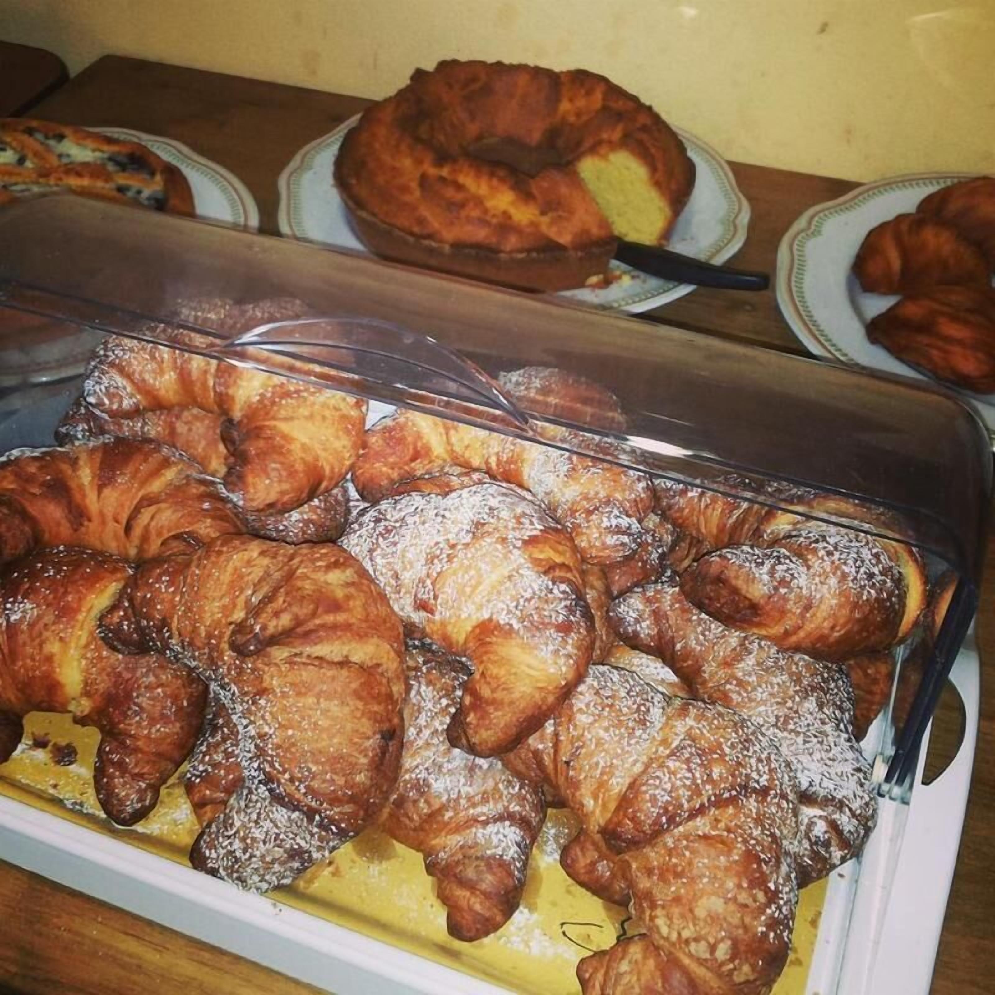 Una vetrina piena di dolci assortiti, tra cui croissant e una torta bundt.