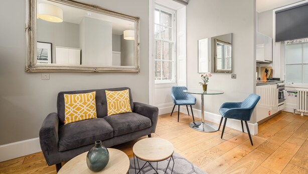 A modern living room with a grey sofa, two chairs, a small table, and a large mirror. - Destiny Scotland - St. Andrew Square Apartments (Edinburgh)