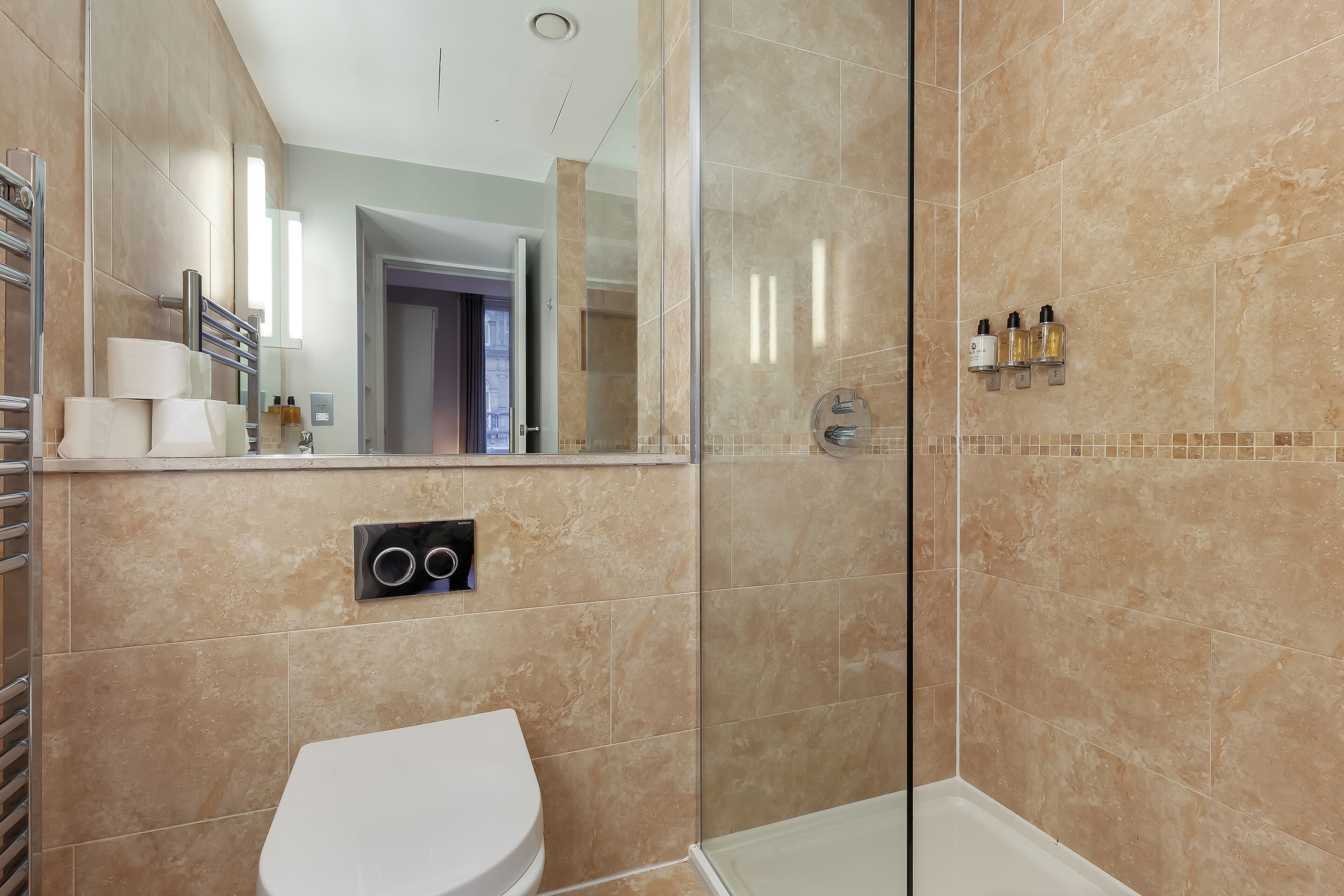 Een moderne badkamer met een douchecabine van glas, een wit toilet en een spiegel die een gang weerkaatst.