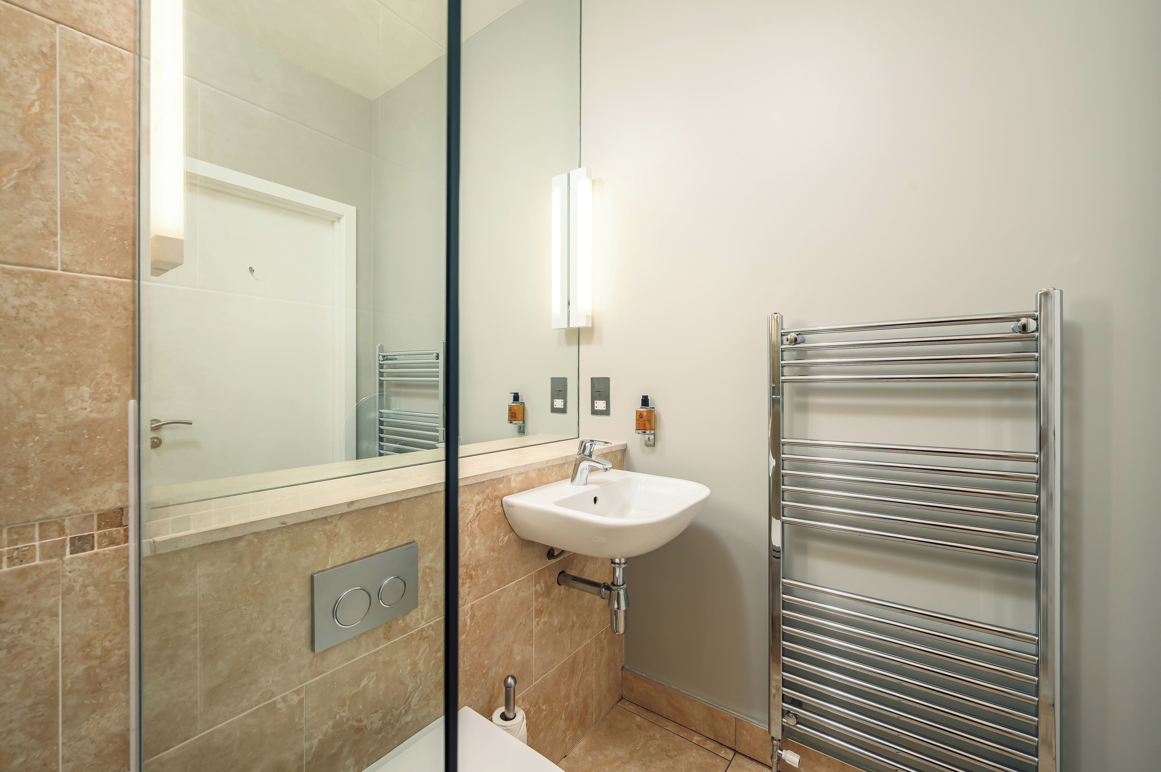 A modern bathroom with a glass shower enclosure, a white sink, and a towel rack.
