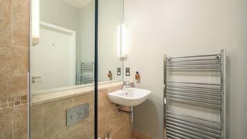 A modern bathroom with a glass shower enclosure, a white sink, and a towel rack.