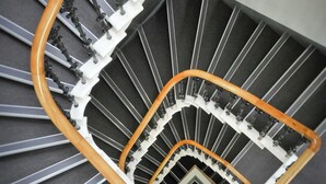 A spiral staircase with a wooden handrail and black balusters, leading to an upper floor. - Destiny Scotland - St. Andrew Square Apartments (Edinburgh)