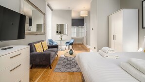 A modern hotel room with a large bed, a sofa, a TV, a desk, and a mirror. - Destiny Scotland - St. Andrew Square Apartments (Edinburgh)