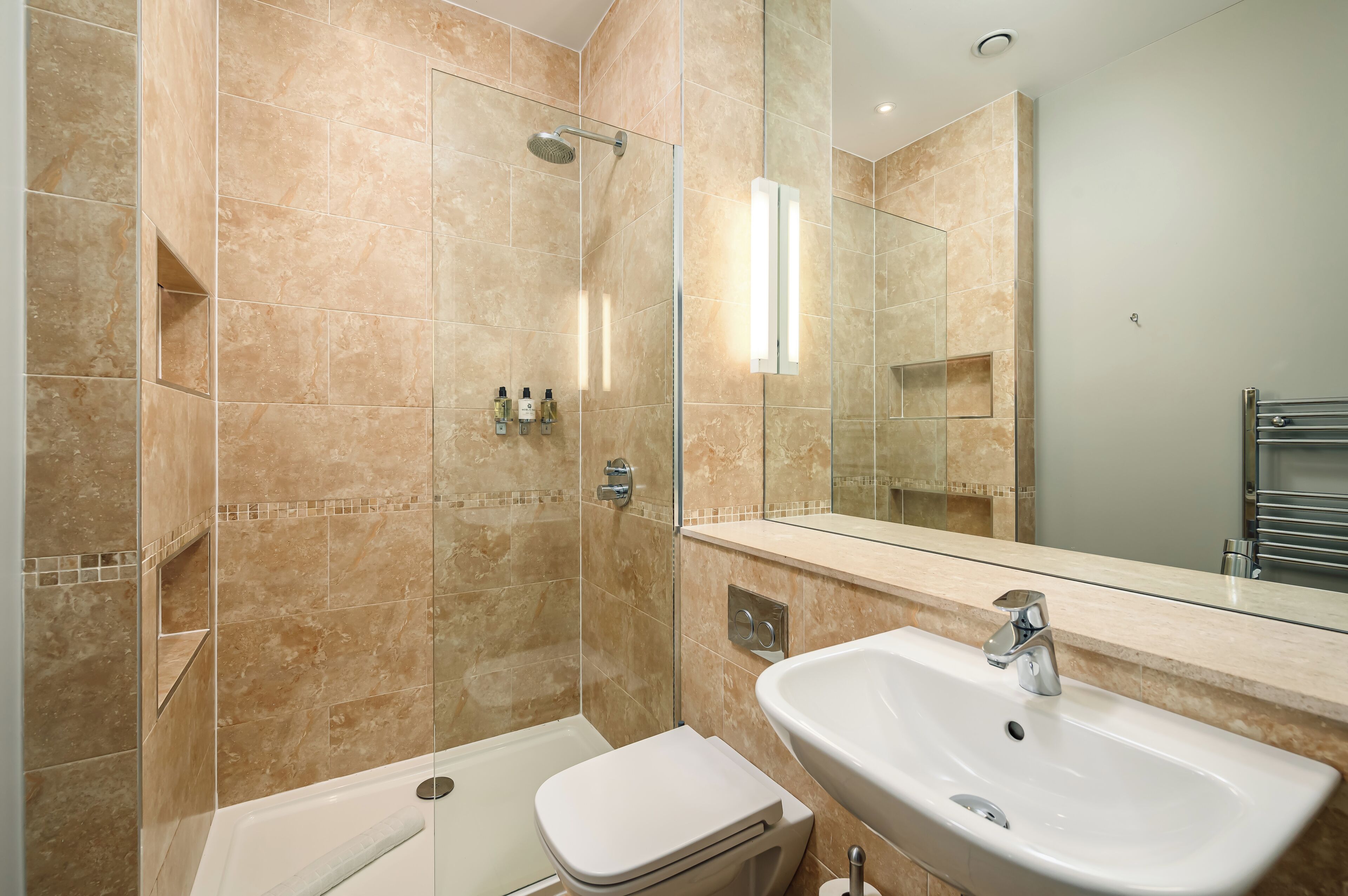 Une salle de bain moderne avec une douche à parois de verre, des toilettes blanches et un lavabo surmonté d’un miroir.