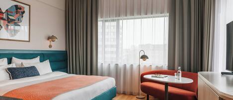 Habitación de hotel con cama, escritorio, silla, mesa, lámpara y ventana con cortinas.