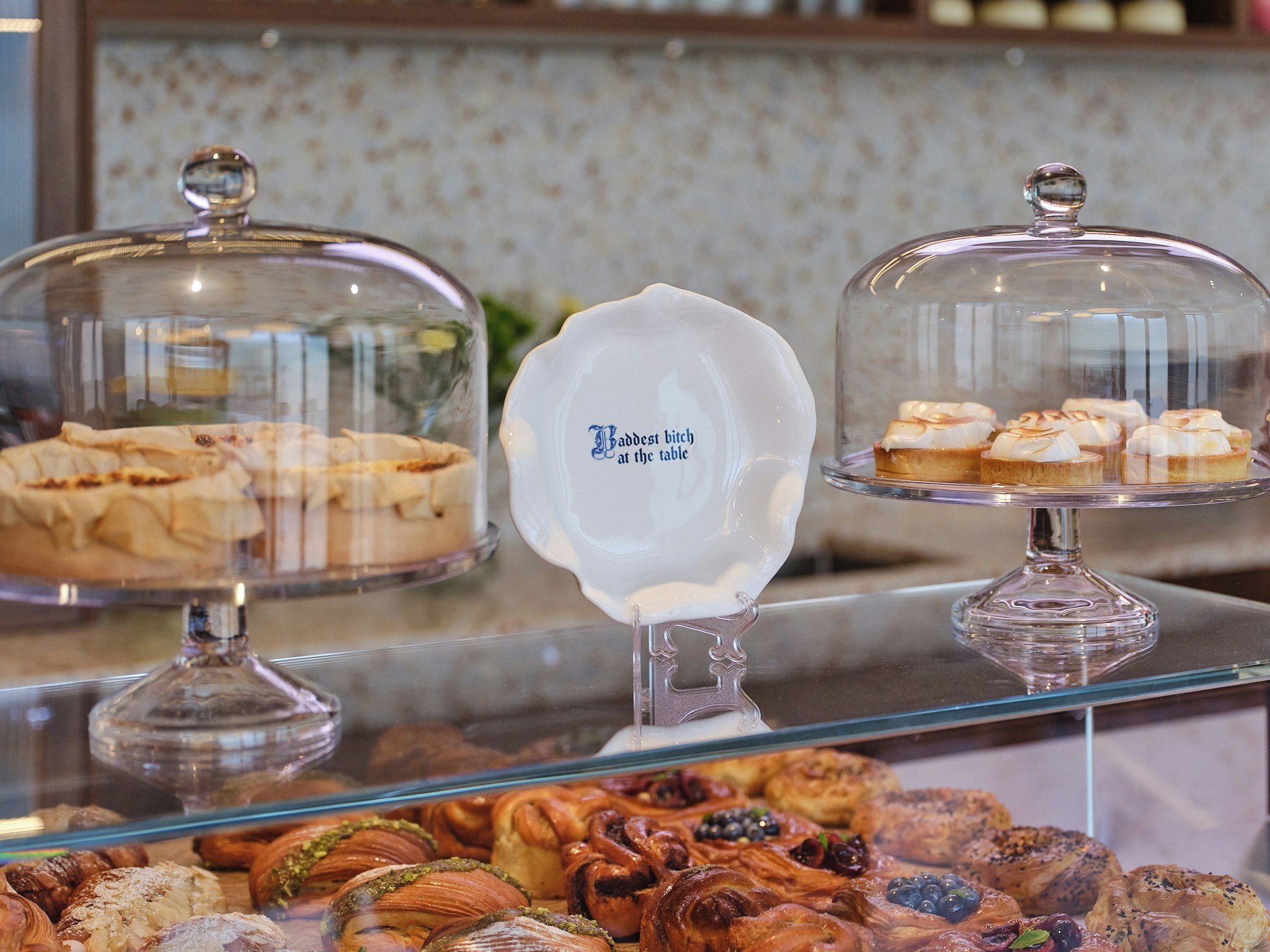 A display case with various pastries and desserts, including a sign that reads 'Badest bitch at the table.'