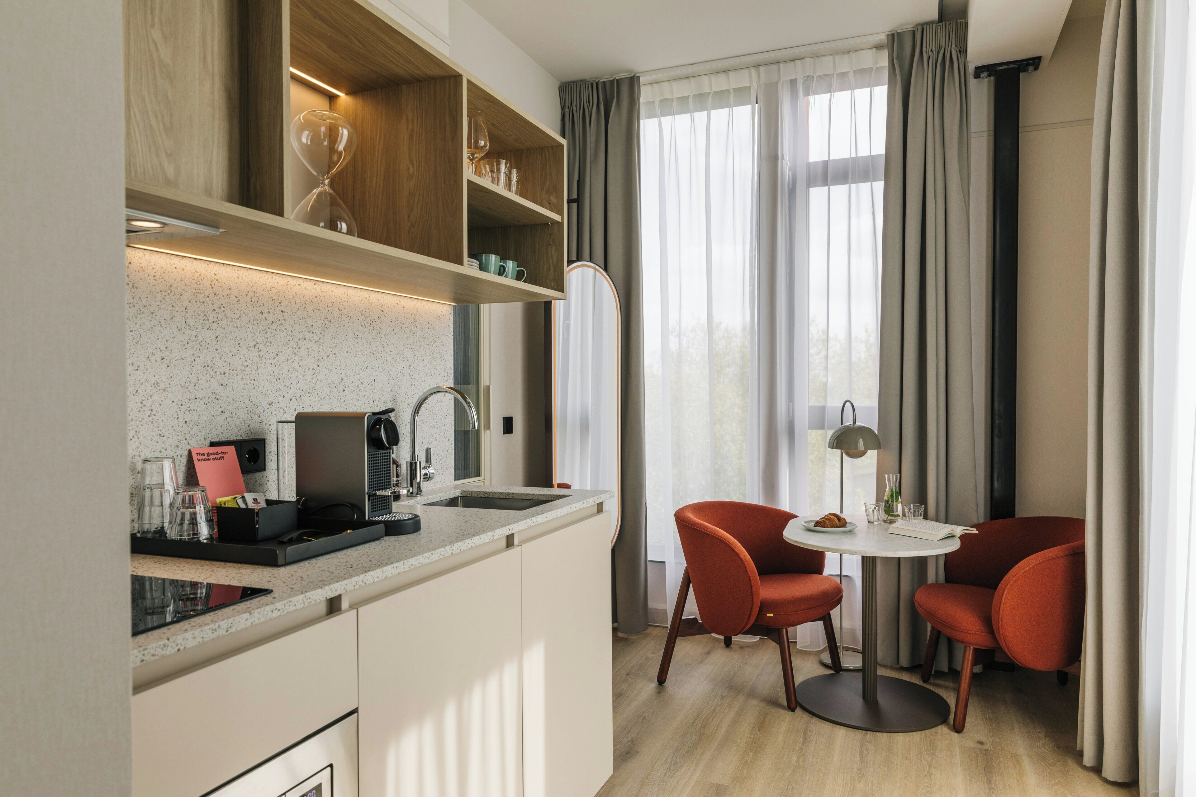 Cocina compacta con cafetera integrada, una pequeña mesa de comedor con dos sillas y un espejo grande sobre el mostrador.