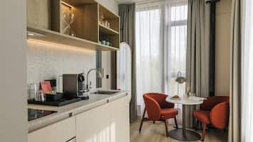 Cocina compacta con cafetera integrada, una pequeña mesa de comedor con dos sillas y un espejo grande sobre el mostrador.