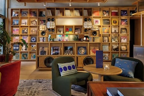 Een kamer met een boekenplank vol vinylplaten, een groene fauteuil, een ronde houten tafel en een rode bank.