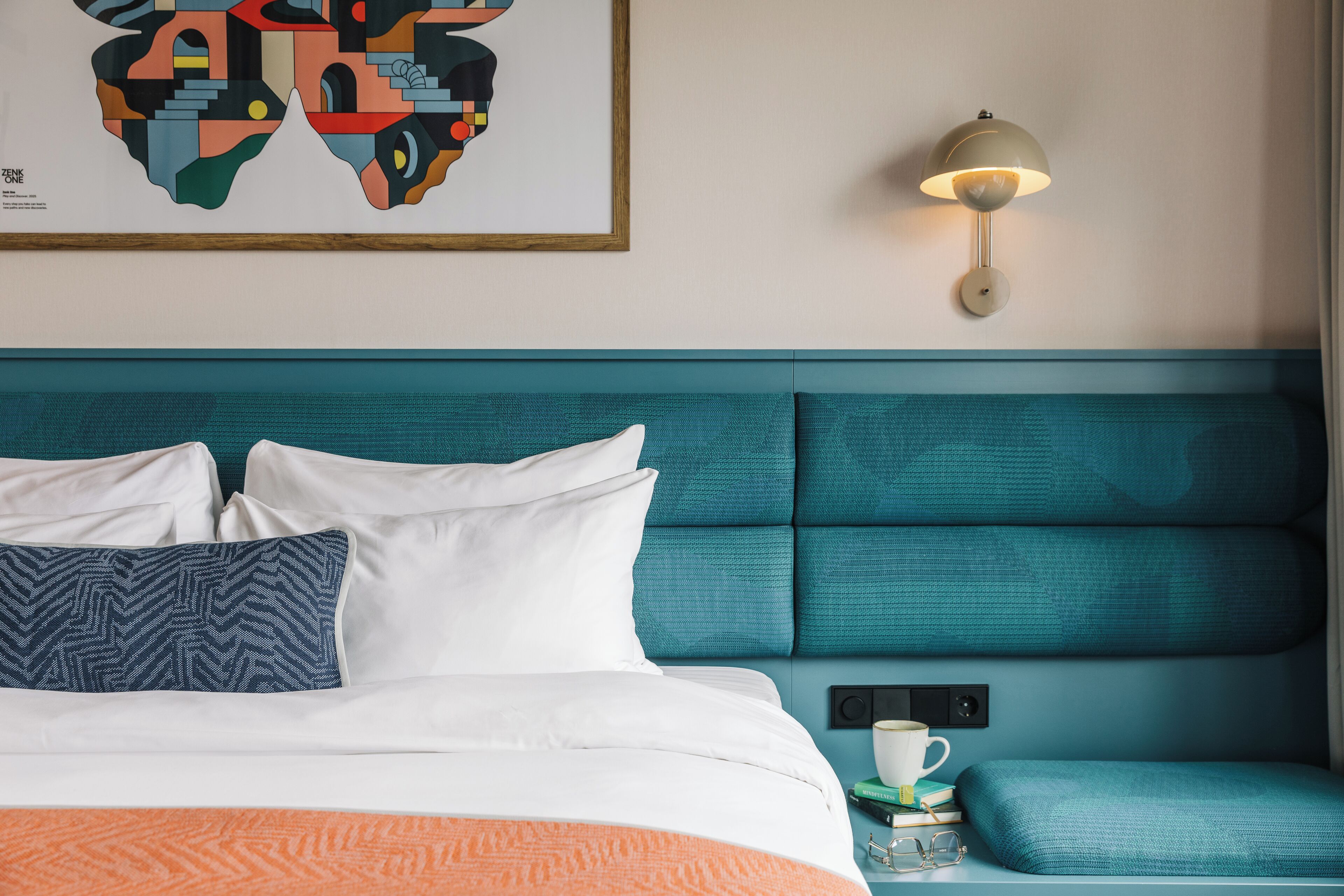 A neatly made bed with white and blue pillows, a teal headboard, and a wall-mounted lamp.