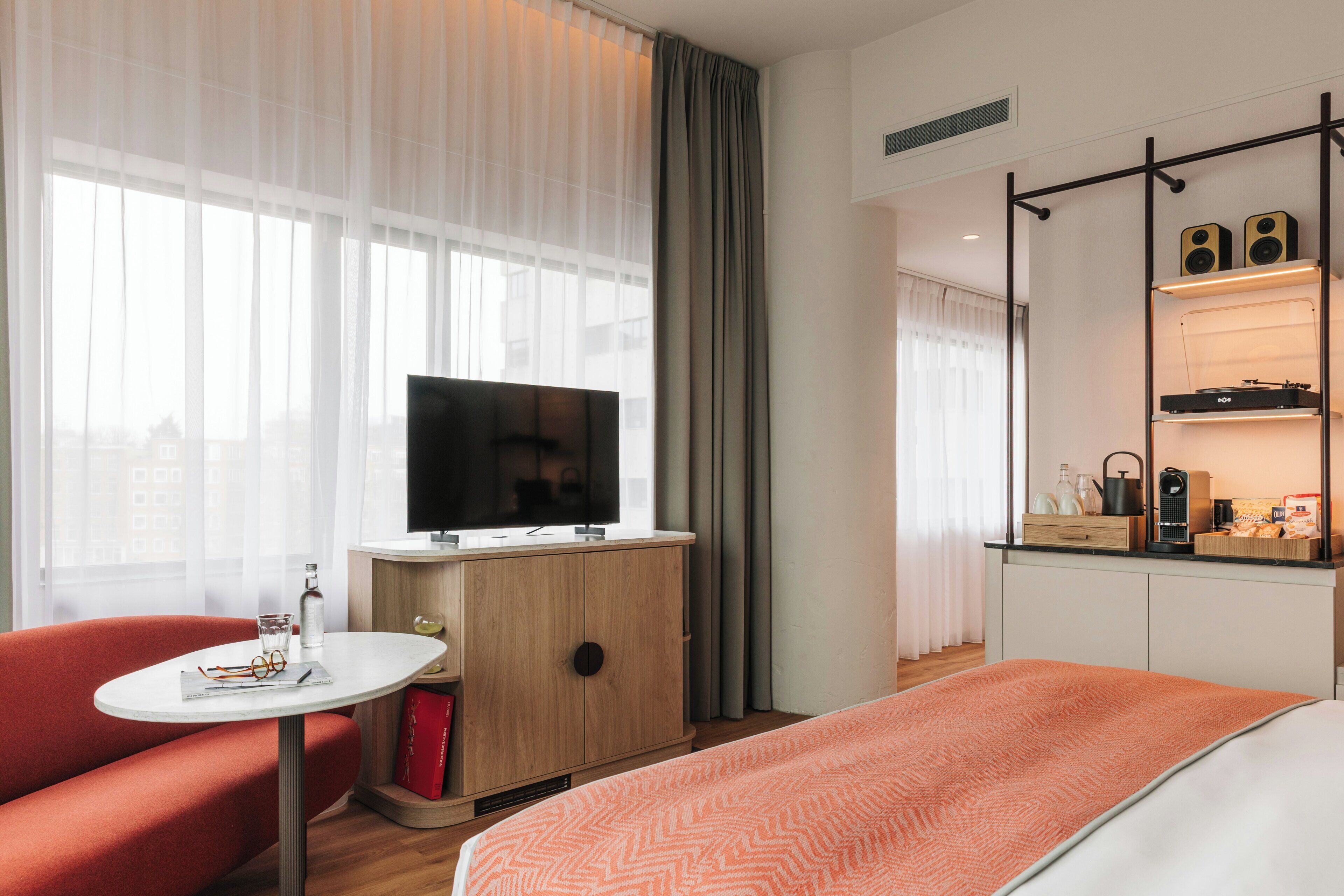 Une chambre d’hôtel comprenant un lit, une télévision, un bureau avec une chaise, une petite table et un coin cuisine.
