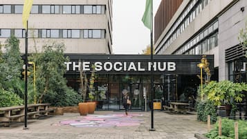 A building entrance with a sign reading 'The Social Hub,' surrounded by outdoor seating and greenery.