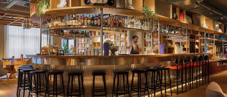 Zona de bar con mostrador curvo, varias estanterías con botellas y taburetes.