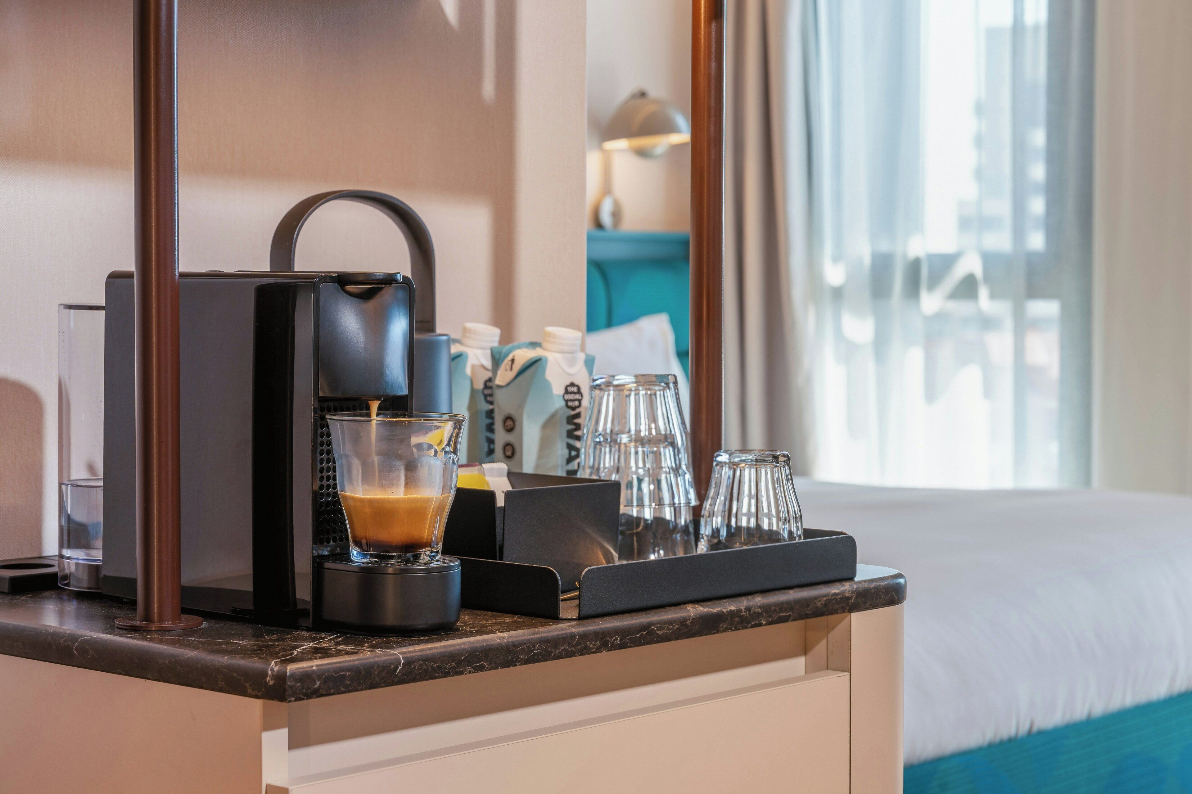 A hotel room's minibar with a coffee maker, a glass of coffee, and a bottle of water.