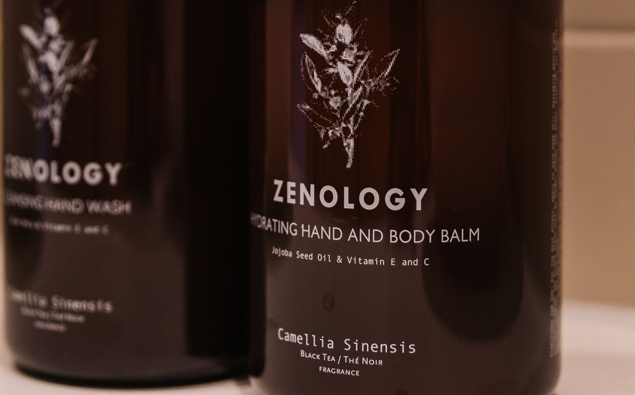Un flacon de baume pour les mains et le corps de la marque Zenology, orné d’un motif floral.