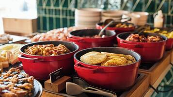 Una mesa de buffet con diversos alimentos en ollas rojas y un pastel en un plato.