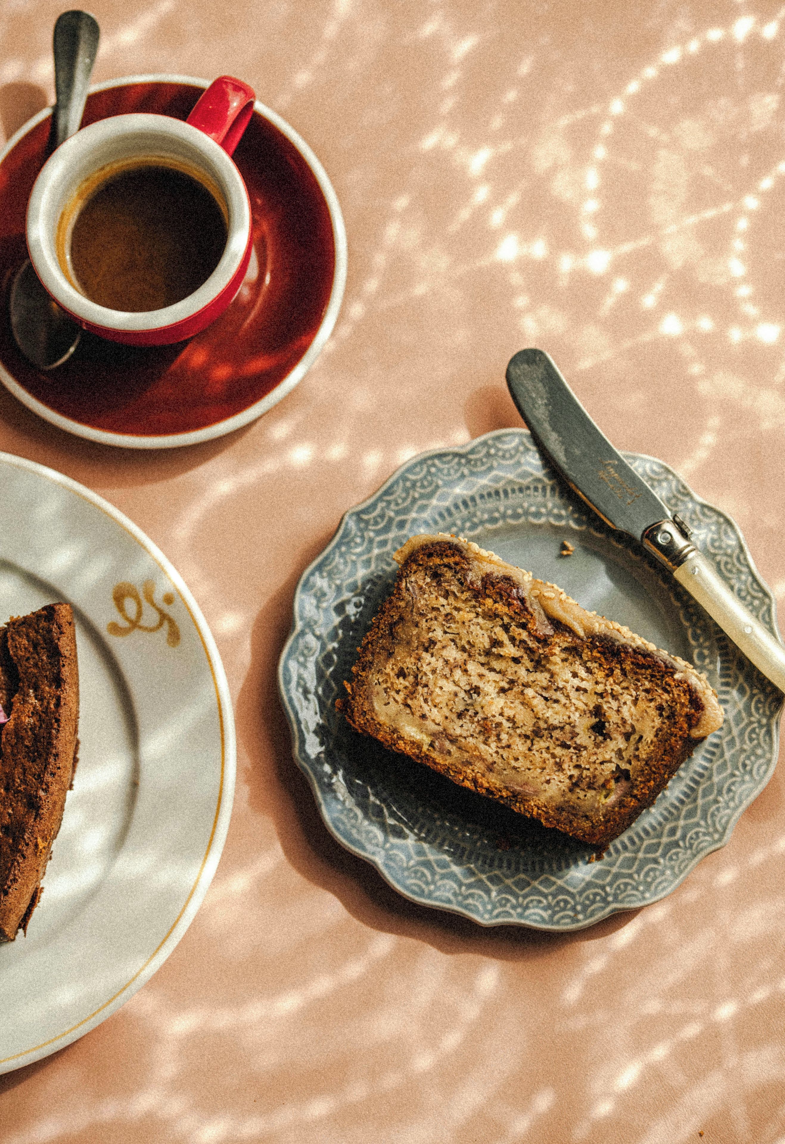 A slice of cake on a plate with a knife, a cup of coffee, and a saucer on a table.