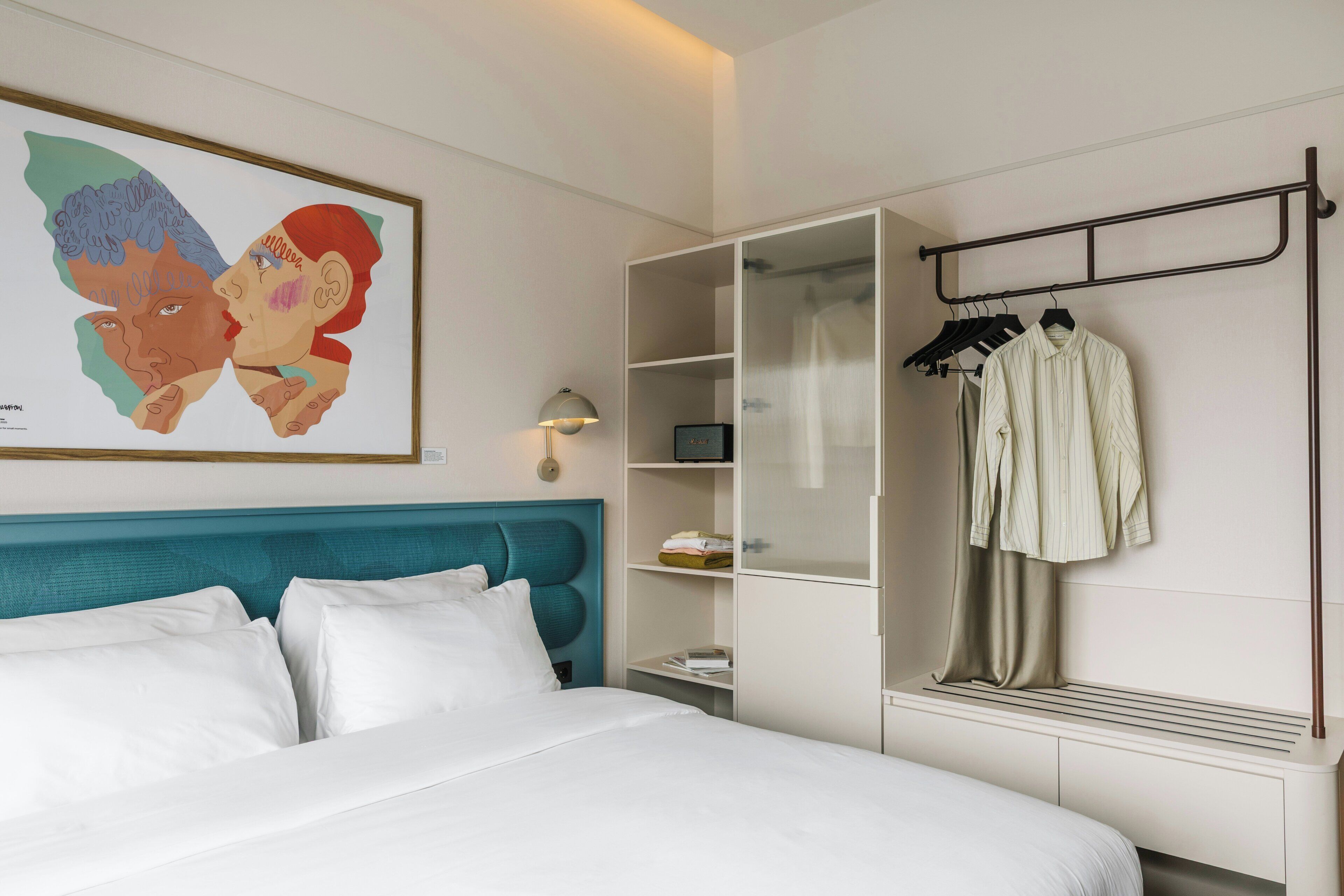 Une chambre d’hôtel comprenant un lit, une armoire, un porte-manteau et une œuvre d’art encadrée accrochée au mur.