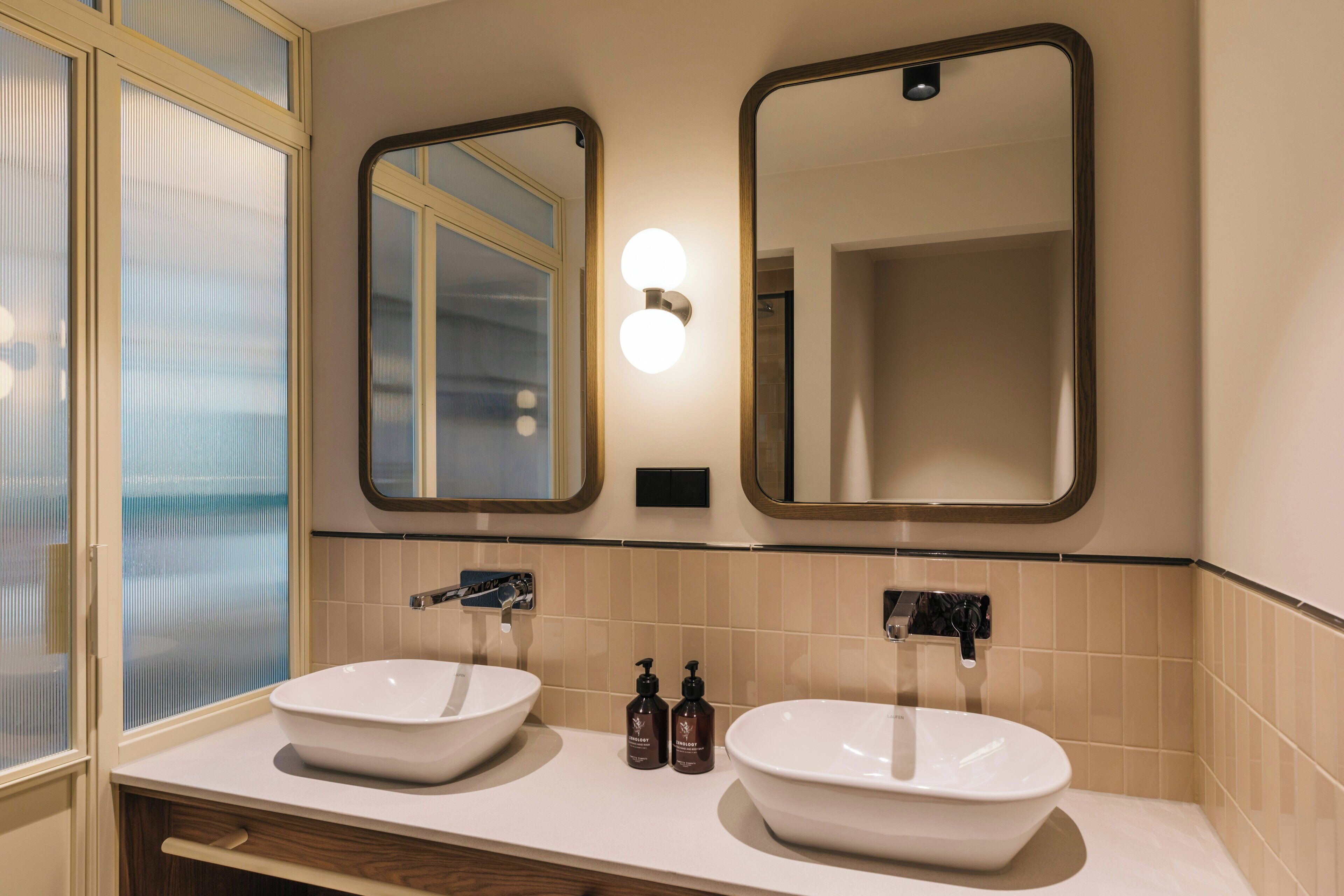 Un baño con dos lavamanos, un espejo y una ventana esmerilada.