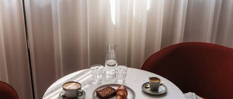 Una mesa redonda con un croissant, un vaso de agua, un vaso de agua helada y una taza de café.